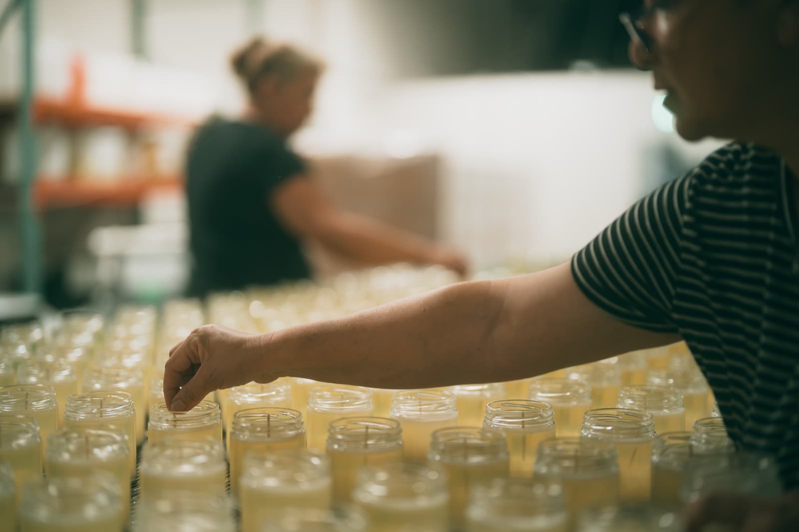 Hands setting wicks across rows of candles at the Lumient factory